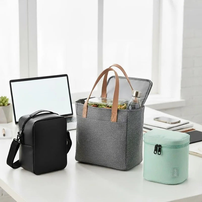 Ensemble de sacs isothermes de différentes tailles et couleurs sur un bureau lumineux, idéal pour transporter repas et boissons au bureau.