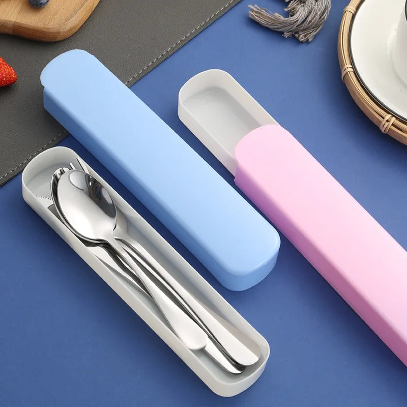 Boîtes de rangement bleu et rose contenant des couverts en acier inoxydable (cuillère, fourchette, couteau), posées sur un fond bleu, parfaites pour le transport des repas.