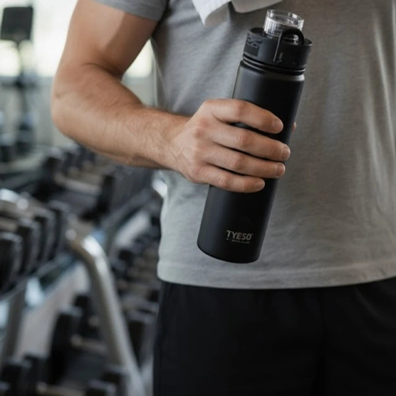 Bouteille isotherme en inox noir mat TYESO tenue à la main à la salle de sport, idéale pour garder l’eau ou les boissons énergétiques à bonne température pendant l’entraînement.