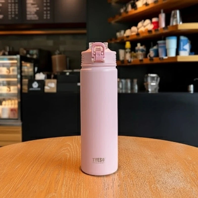 Bouteille isotherme en inox rose TYESO posée sur une table de café, bouchon sport anti-fuite, design élégant et féminin, idéale pour garder les boissons chaudes ou froides plusieurs heures.