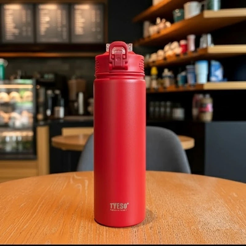 Bouteille isotherme inox rouge TYESO posée sur une table de café, design moderne avec bouchon sport anti-fuite, idéale pour boissons chaudes ou froides.