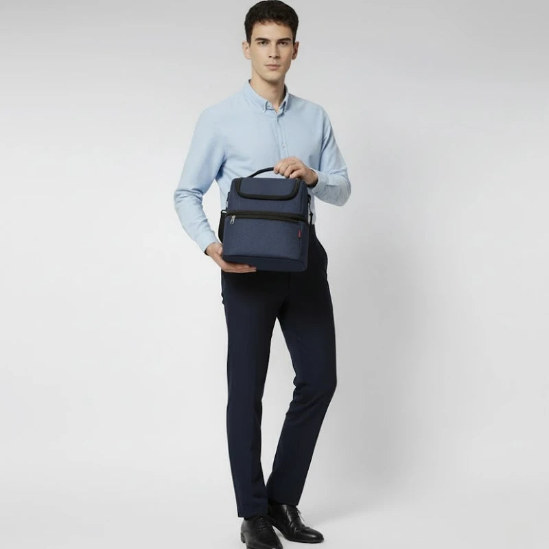 Homme debout tenant un sac isotherme bleu devant lui, en chemise claire et pantalon foncé.