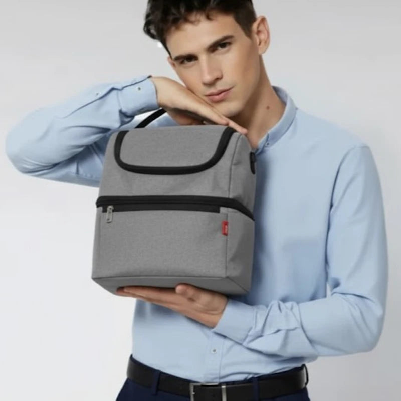Homme en chemise claire présentant un sac isotherme gris en plan portrait.