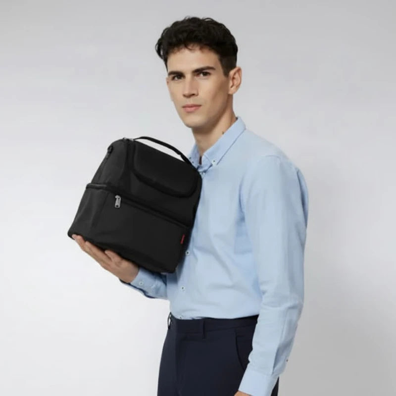 Homme tenant un sac isotherme noir contre lui, en chemise bleue, sur fond neutre.