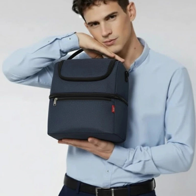 Homme tenant un sac isotherme bleu devant lui, en tenue de bureau, sur fond neutre.