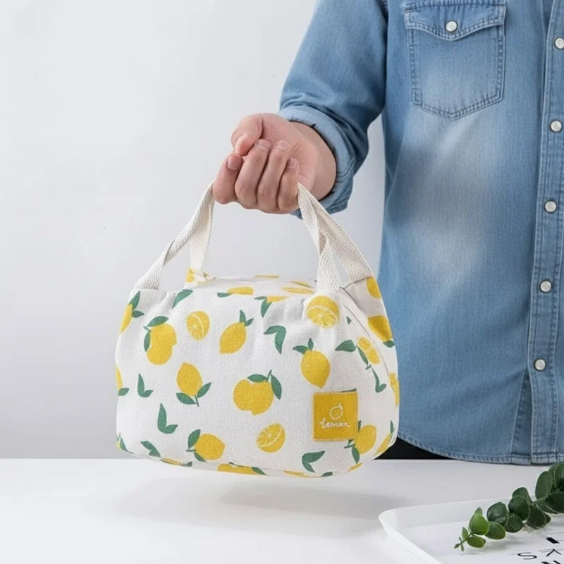 Sac isotherme repas à imprimé citrons, présenté en main devant une chemise en jean pour illustrer sa taille compacte et son design naturel.