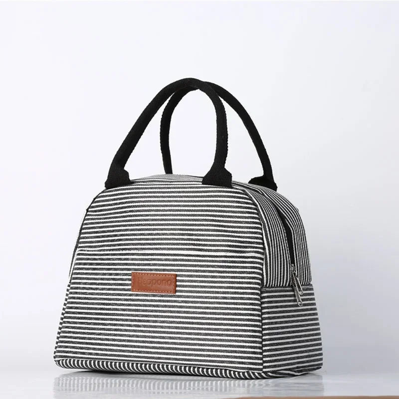 Lunch Bag à rayures noir et blanc vu de face, doté de poignées noires et d’une étiquette marron, idéal pour garder les repas frais avec style posé sur fond clair.