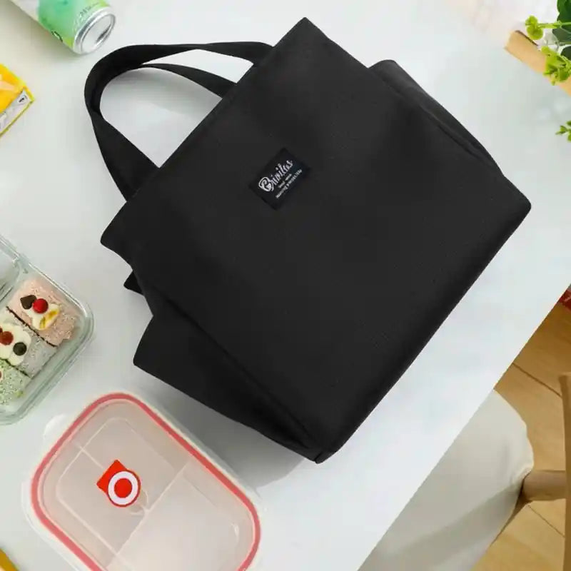 Vue de dessus d’un lunch bag sac isotherme noir posé sur une table, avec une lunch box repas à côté, idéal pour déjeuner au bureau.