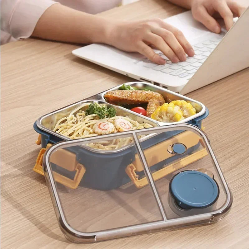 Lunch box isotherme en inox bleu à trois compartiments, remplie d’un repas équilibré avec pâtes, légumes et poulet, posée sur un bureau à côté d’un ordinateur portable — parfaite pour déjeuner au travail tout en gardant les aliments chauds ou frais.