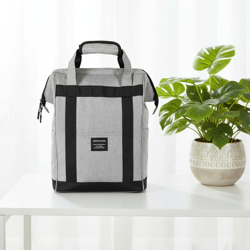 Sac à dos isotherme gris au design moderne posé sur une table blanche, avec une plante décorative en arrière-plan.