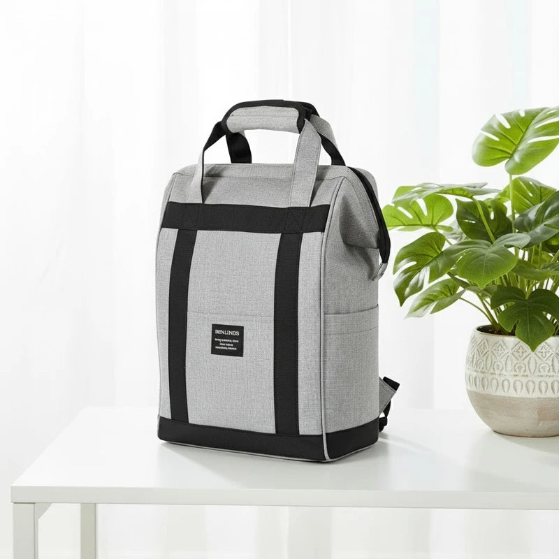 Sac à dos isotherme gris au design vertical posé sur une table blanche, avec une plante décorative en arrière-plan.