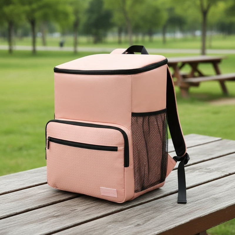 Sac à dos isotherme rose posé sur une table en bois en extérieur, avec poche avant zippée et filet latéral, idéal pour pique-niques et déplacements.