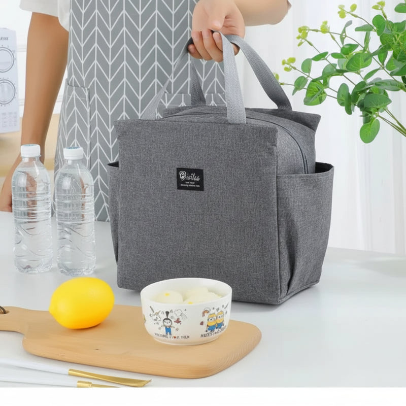 Sac isotherme repas gris avec poignées, posé sur une table de cuisine, utilisé pour transporter un déjeuner avec bouteilles d’eau, bol et citron, format compact et élégant.
