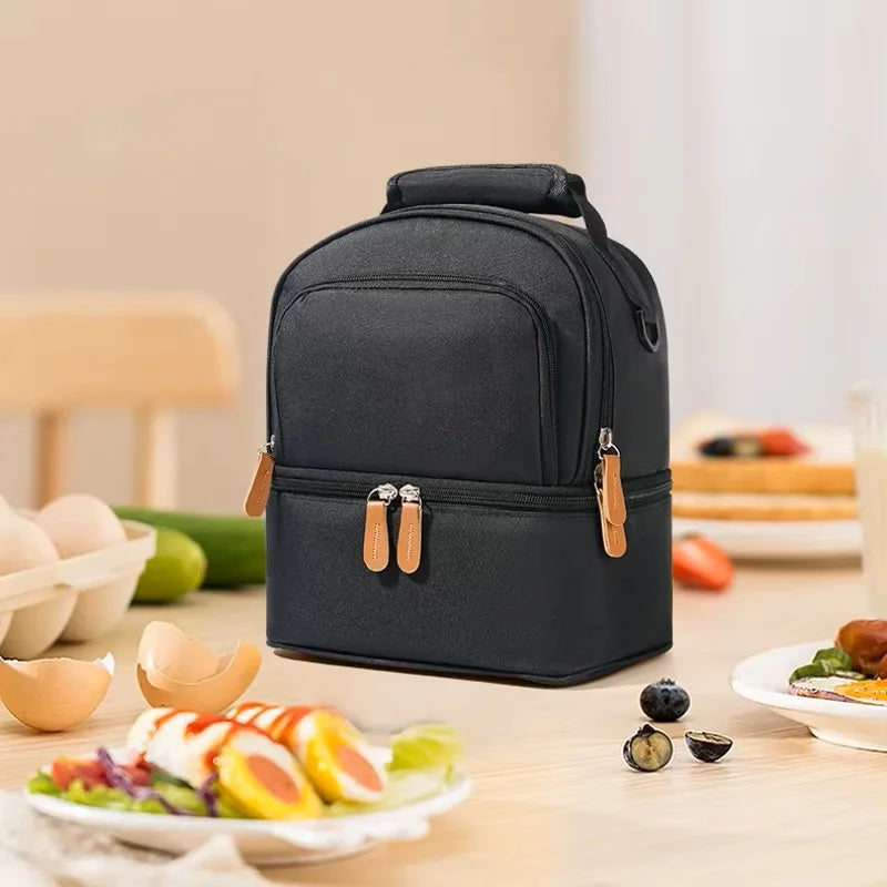 Sac isotherme bébé biberon noir à double compartiment, posé sur une table avec des aliments, adapté au transport du biberon et des repas lors des sorties.