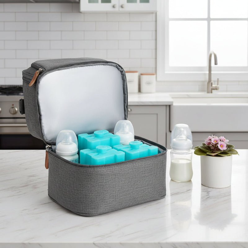 Sac isotherme gris ouvert contenant des pains de glace et des biberons, posé sur un plan de travail en cuisine.