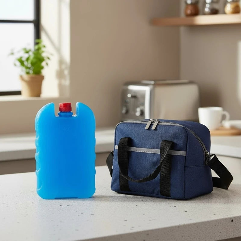Sac isotherme bleu marine posé sur un plan de travail avec un pain de glace bleu vif à côté, dans une cuisine lumineuse moderne.