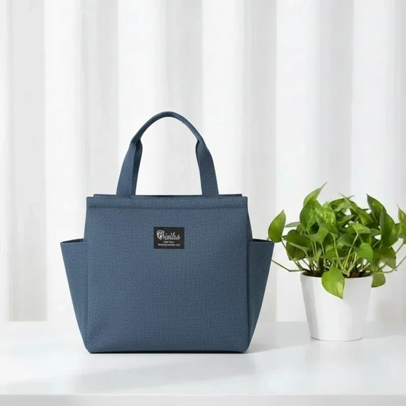 Sac isotherme bleu type lunch bag posé sur une table blanche avec une plante en arrière-plan