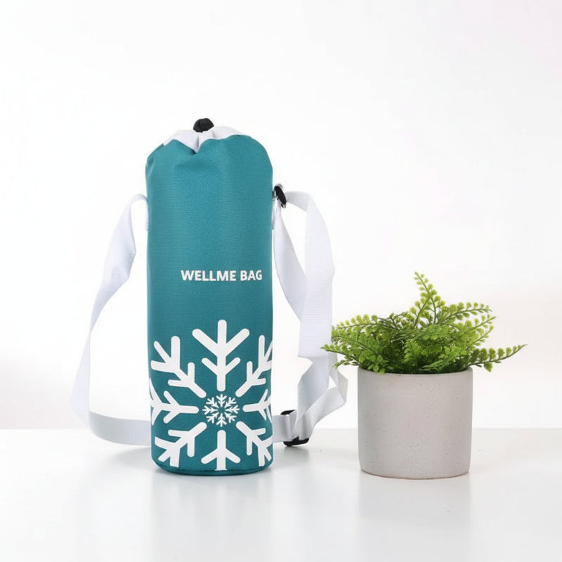 Sac isotherme pour bouteille bleu avec motif flocon blanc et bandoulière, posé sur une table blanche à côté d’une plante.