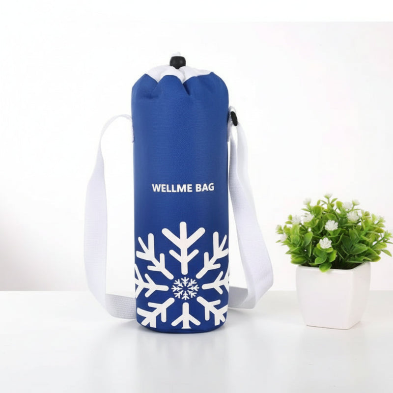 Sac isotherme pour bouteille bleu avec motif flocon blanc et bandoulière, posé sur une table blanche à côté d’une plante.