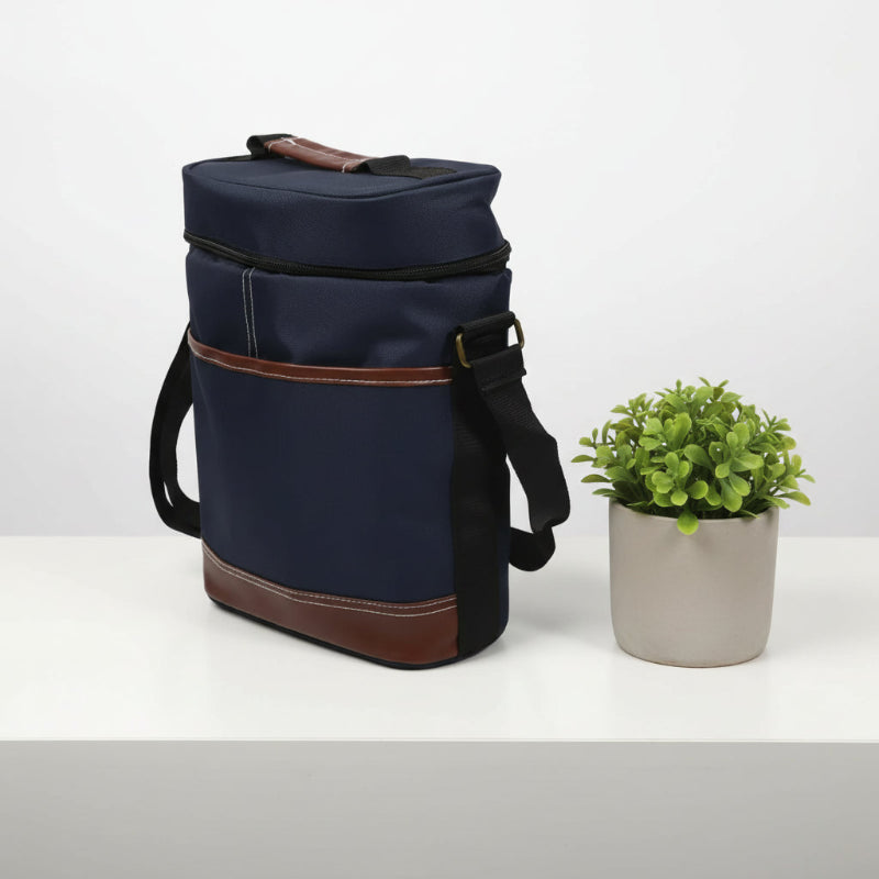 Sac isotherme pour bouteille bleu marine avec finitions cuir marron vu de côté, posé sur une table avec une petite plante décorative.