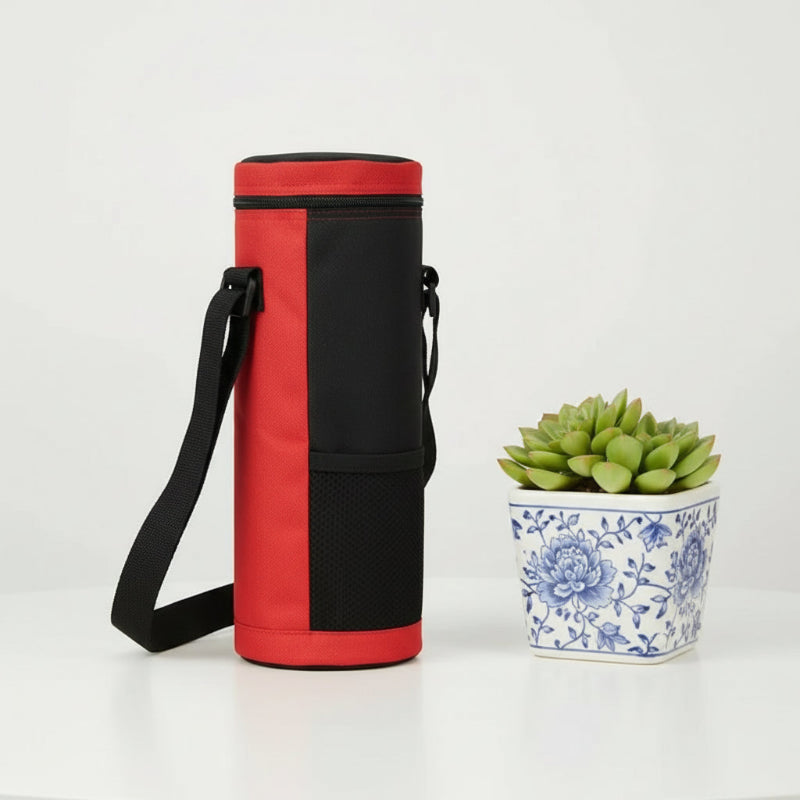 Sac isotherme pour bouteille rouge vu de côté, avec sangle noire, posé sur une table blanche à côté d’une plante décorative.