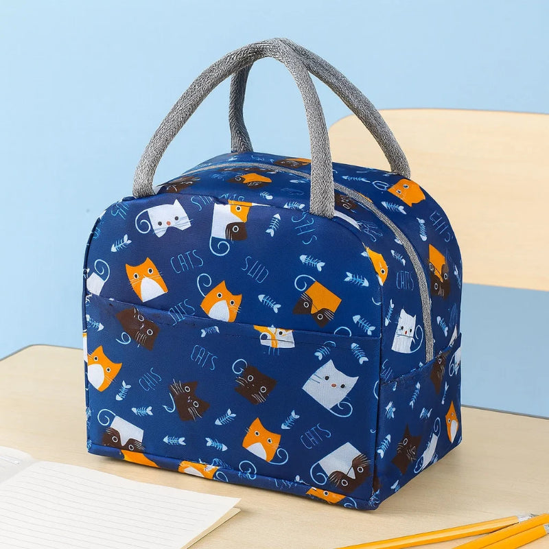 Sac isotherme enfant bleu avec motifs de chats colorés posé sur une table dans une salle de classe.
