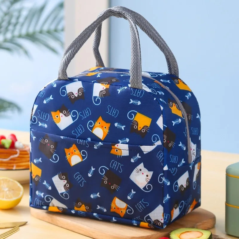 Sac isotherme pour enfant de couleur bleue avec motif de chats colorés, posé sur une table en cuisine.