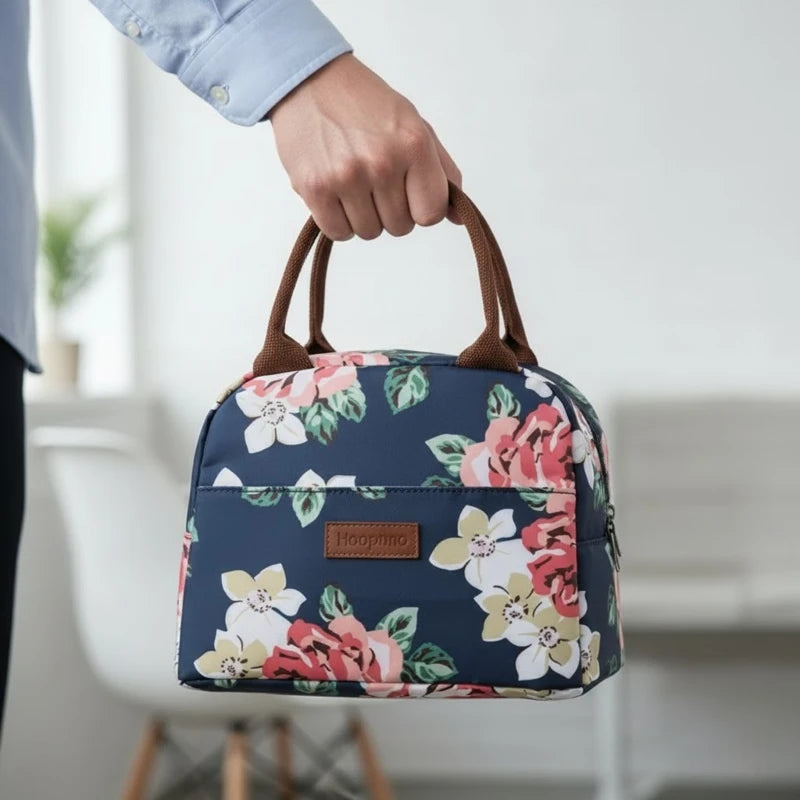 Sac isotherme à motifs fleuris bleu marine tenu à la main, avec poignées marron, dans un intérieur lumineux.
