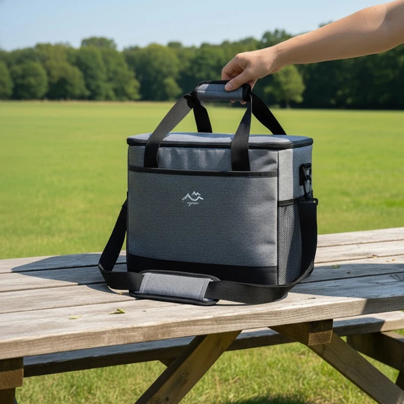 sac isotherme gris et noir posé sur une table en bois, avec une main tenant la poignée, en extérieur dans un parc ensoleillé