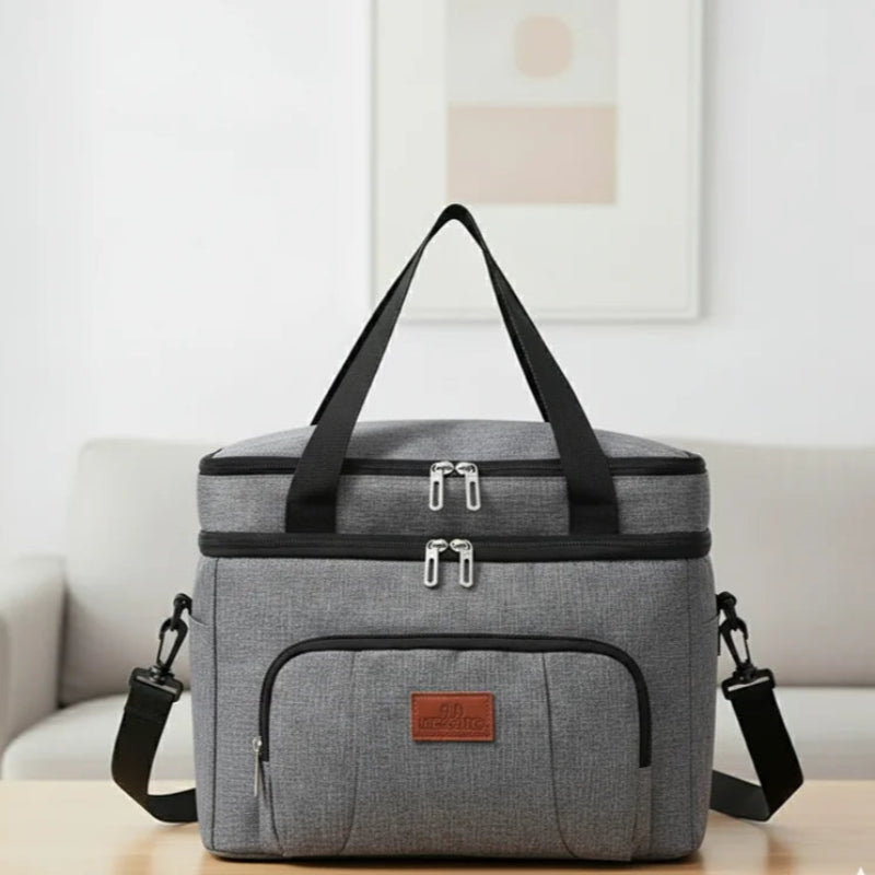 Sac isotherme repas gris avec bandoulière et poignées noires, posé sur une table dans un intérieur moderne, idéal pour transporter déjeuner ou pique-nique.