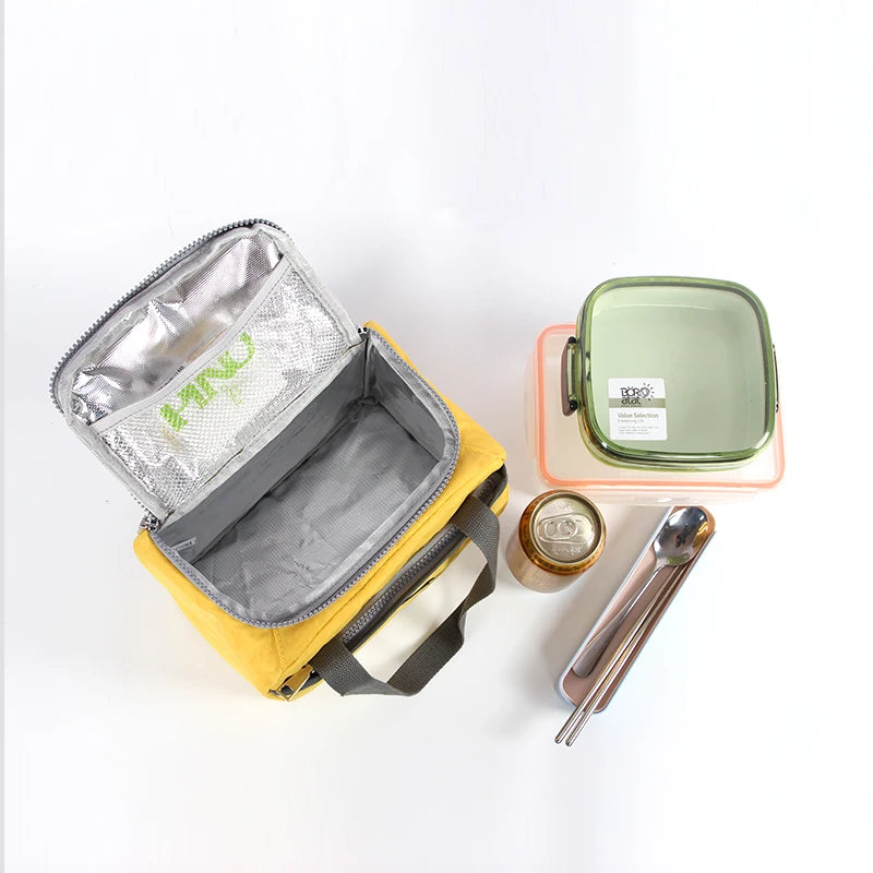 Sac isotherme jaune ouvert vu du dessus, accompagné d’une lunch box, d’une boisson et de couverts, idéal pour transporter un repas complet.