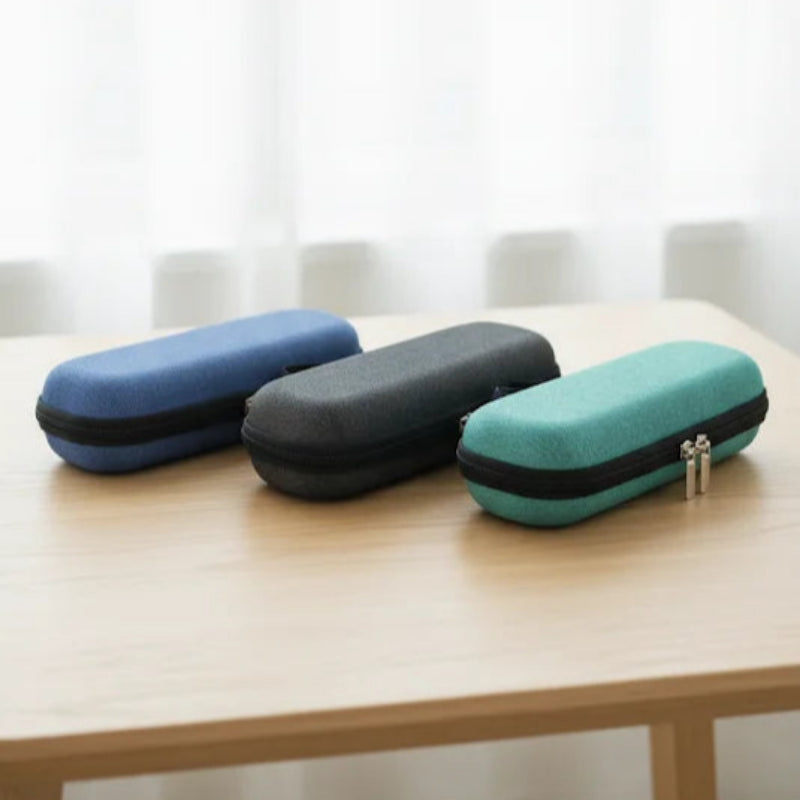 Trois pochettes isothermes médicales fermées, posées côte à côte sur une table en bois clair : une bleue, une noire et une verte, devant un fond clair avec rideaux.