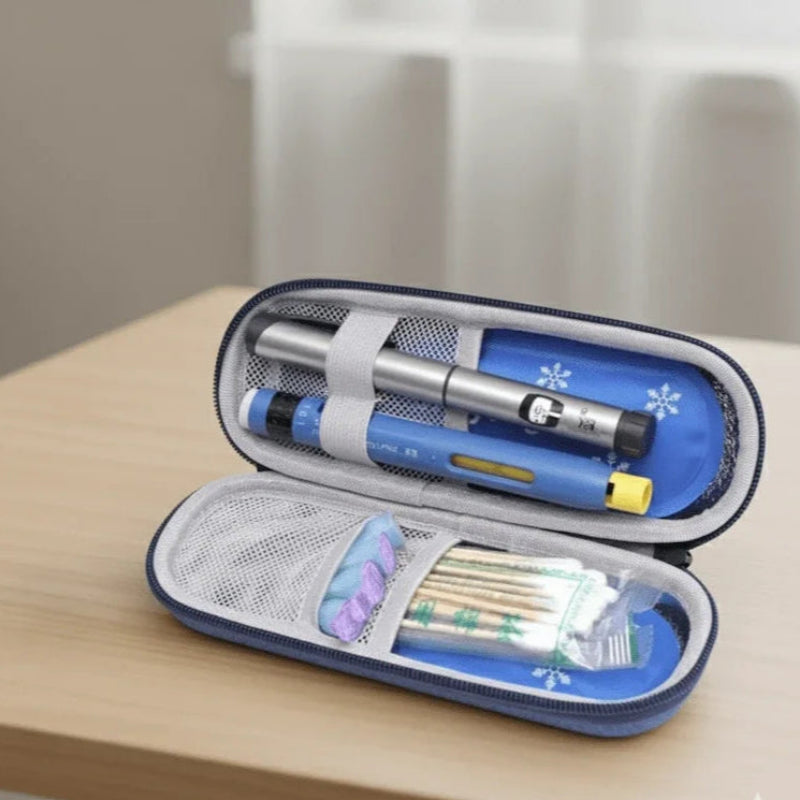 Étui isotherme médical bleu ouvert, contenant deux stylos injecteurs d’insuline fixés par des sangles élastiques et des accessoires de soins dans des pochettes en filet, posé sur une table en bois clair.