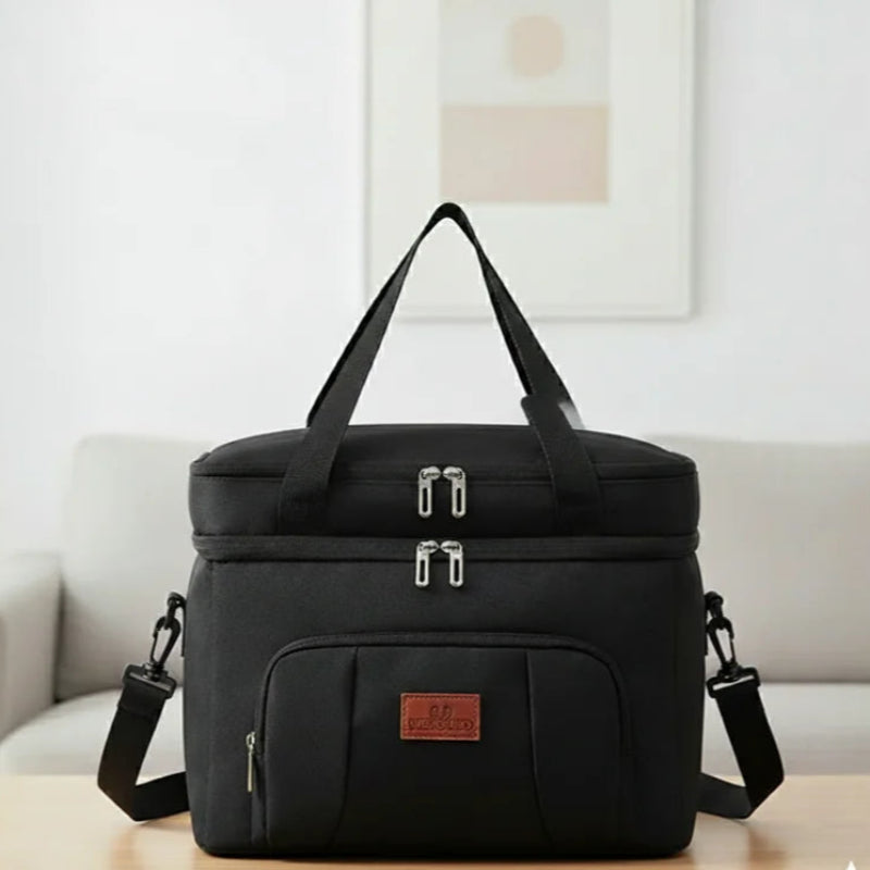 Sac isotherme repas noir avec bandoulière et poignées noires, posé sur une table dans un intérieur moderne, idéal pour transporter déjeuner ou pique-nique.