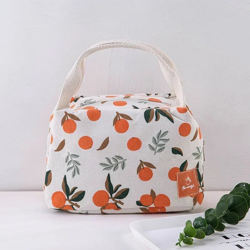 Sac isotherme en toile beige à motifs d’oranges et de feuilles vertes, avec poignées en coton tissé, posé sur une table claire.