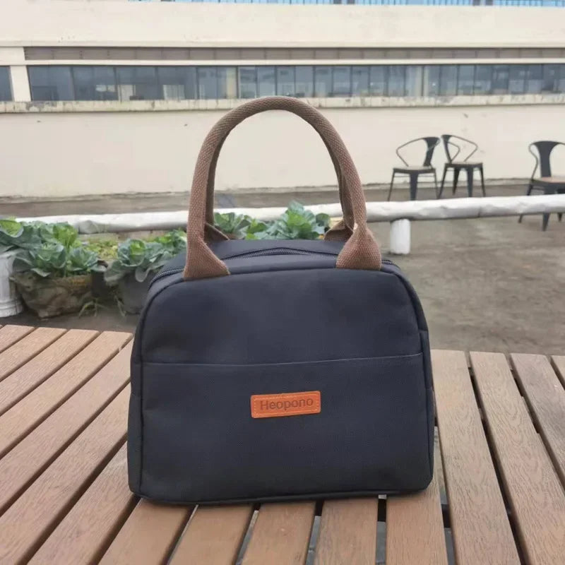 sac isotherme repas bleu marine vu de face, posé sur une table de pique-nique en bois, avec poignées marron et étiquette en cuir
