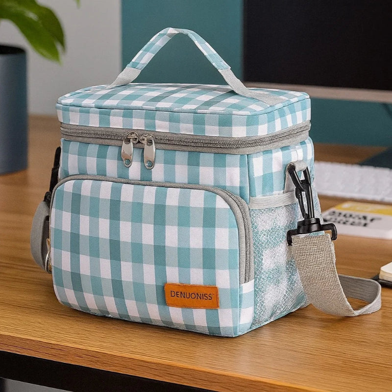 Sac isotherme repas à carreaux vert et blanc posé sur un bureau en bois, avec sangle grise et fermeture éclair double, idéal pour le déjeuner au travail.