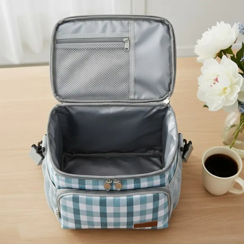 Intérieur du sac isotherme repas à carreaux vert et blanc, doublure argentée propre et spacieuse, posé sur une table avec une tasse de café et un vase de fleurs.