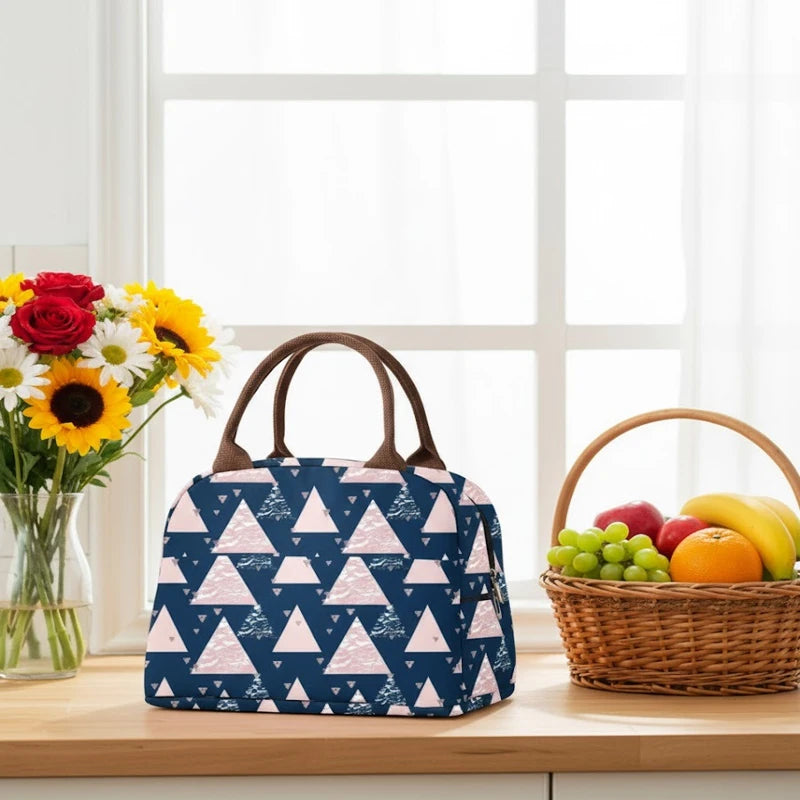 Sac isotherme géométrique bleu marine et rose posé sur un plan de travail, avec fleurs et panier de fruits en arrière-plan.