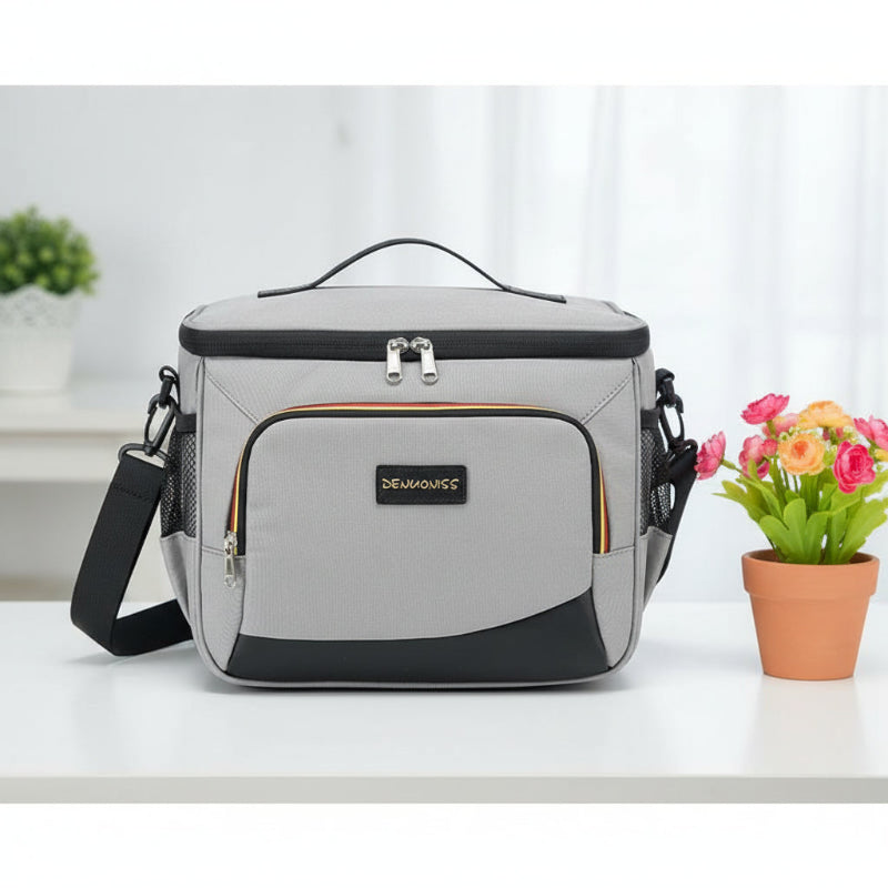 Sac isotherme repas gris posé de face sur une table, avec un pot de fleurs à côté et un second pot de fleurs en arrière-plan.