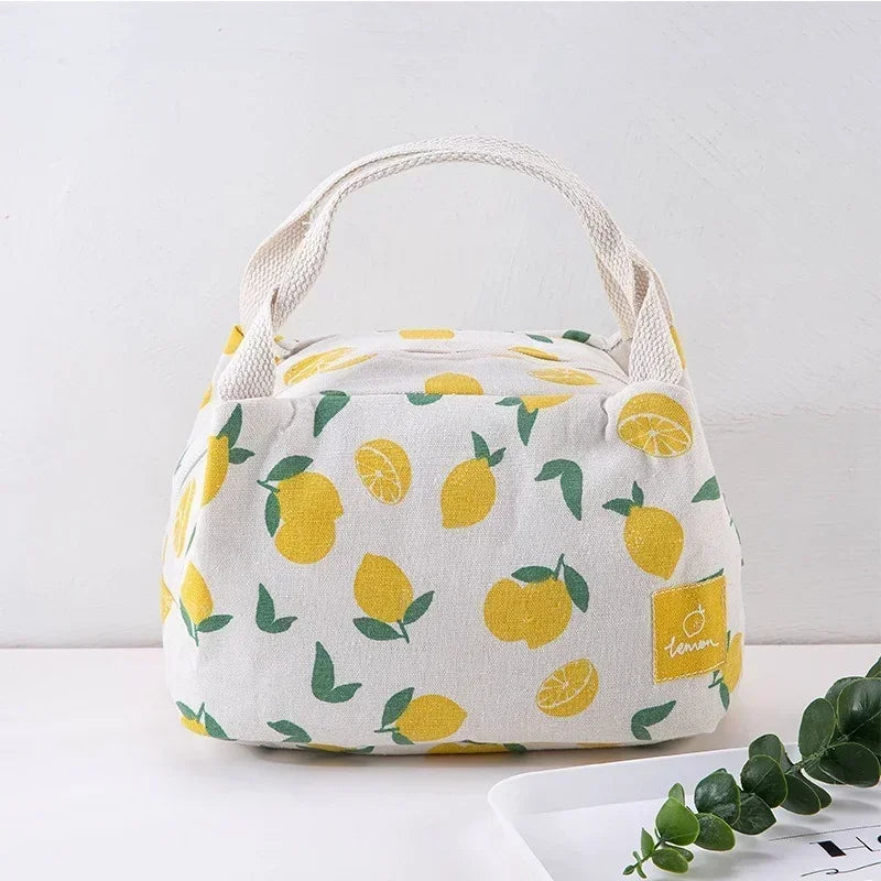 Sac isotherme repas en toile beige avec motif citron jaune et feuilles vertes, muni de deux anses en coton tressé, posé sur une table blanche.