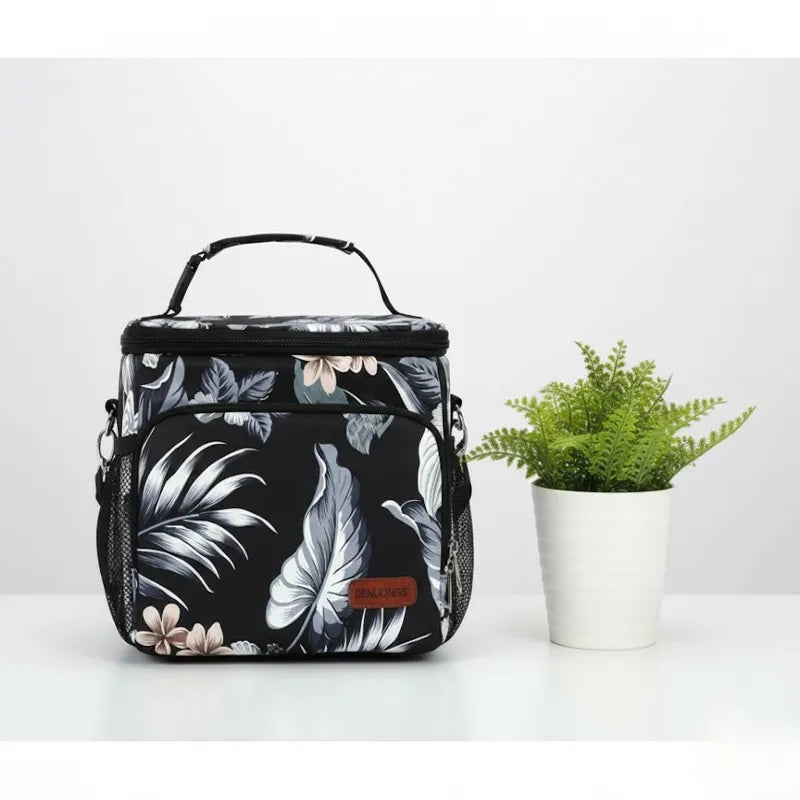 Sac isotherme repas noir à motif floral posé sur une table, idéal pour transporter un déjeuner frais.