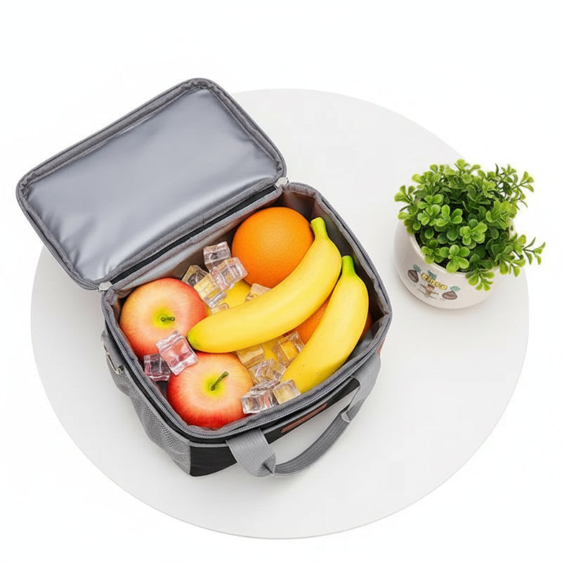 Sac isotherme repas noir et gris ouvert, contenant des fruits et des glaçons, posé sur une table blanche avec une plante.