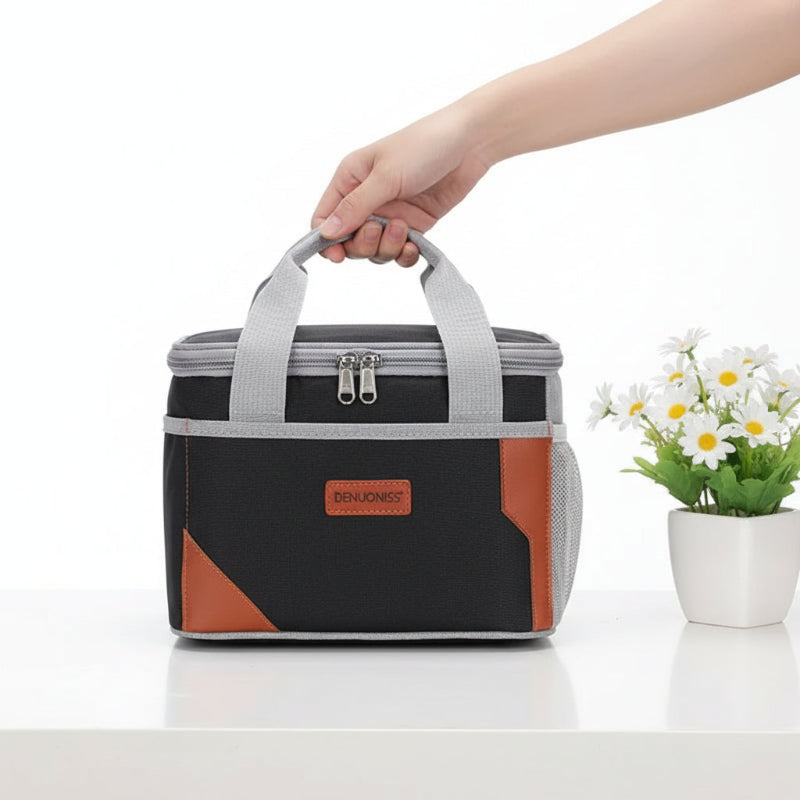 Sac isotherme repas noir et gris tenu par la poignée, posé sur une table blanche avec un pot de fleurs.