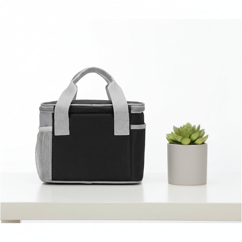 Sac isotherme repas noir et gris vu de dos, posé sur une table blanche à côté d’une petite plante verte.