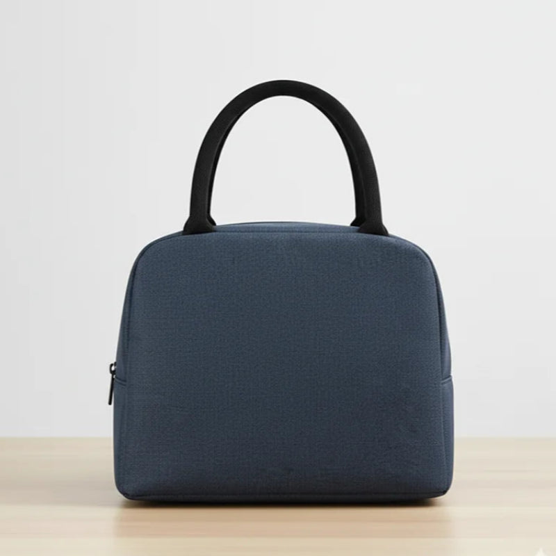 Sac isotherme repas bleu marine, vue de dos. Deux anses noires sur le dessus. Posé sur une table bois clair, fond blanc uni.