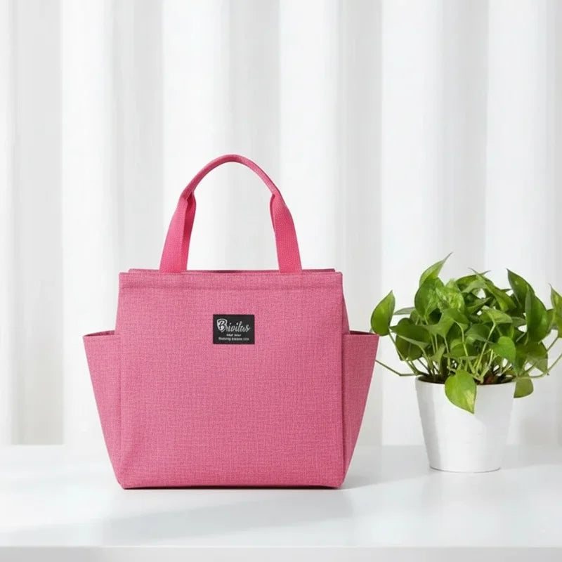 Sac isotherme rose posé sur une table blanche, avec poignées et plante verte en arrière-plan