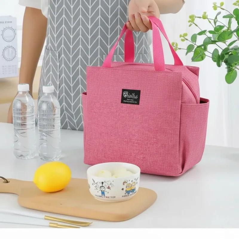 Sac isotherme rose posé sur une table avec repas, bouteilles d’eau et citron, tenu à la main