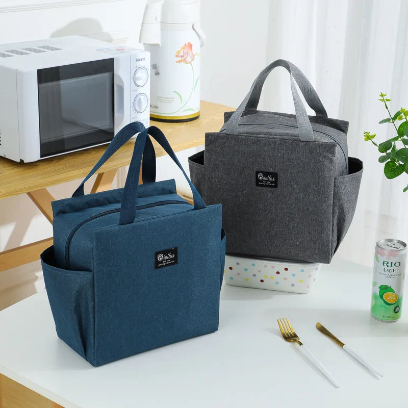 Sacs isothermes bleu et gris posés sur une table, utilisés comme lunch bag pour repas au bureau