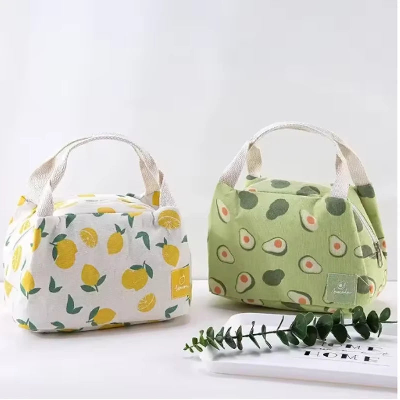 Deux sacs isothermes posés côte à côte sur une table blanche : l’un beige à motifs de citrons jaunes, l’autre vert clair à motifs d’avocats, avec des anses en tissu beige.